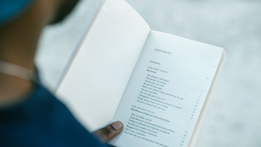 Reader holding an open book to a printed table of contents page with chapter headings
