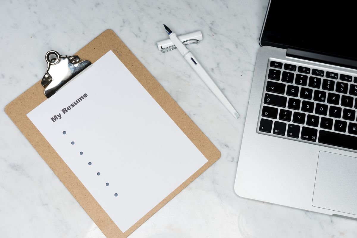 Clipboard with a resume document beside a pen and laptop on a marble desk